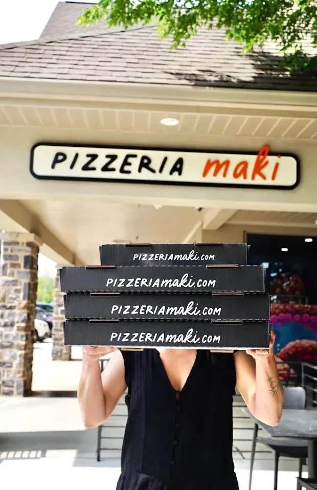 Person holding four pizza boxes in front of the Pizzeria Maki storefront